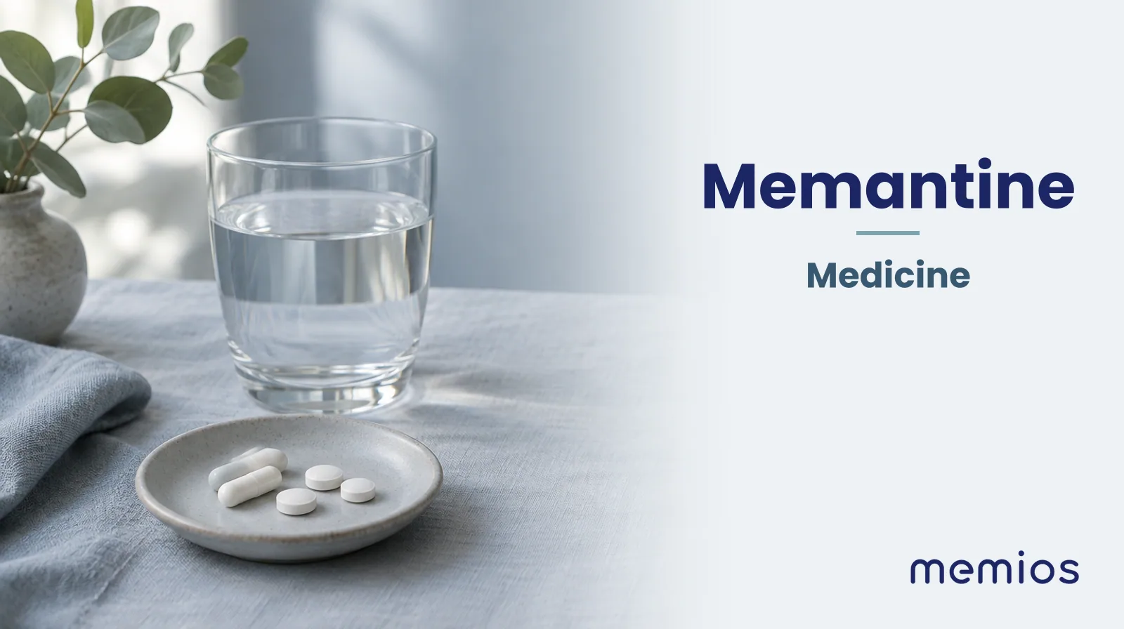 Photograph for Memantine: plain unmarked tablets in a dish beside a glass of water on pale linen.